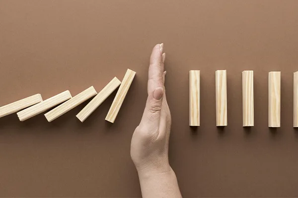 Hand stopping a chain of falling dominoes, representing how to avoid jewelry software implementation failure