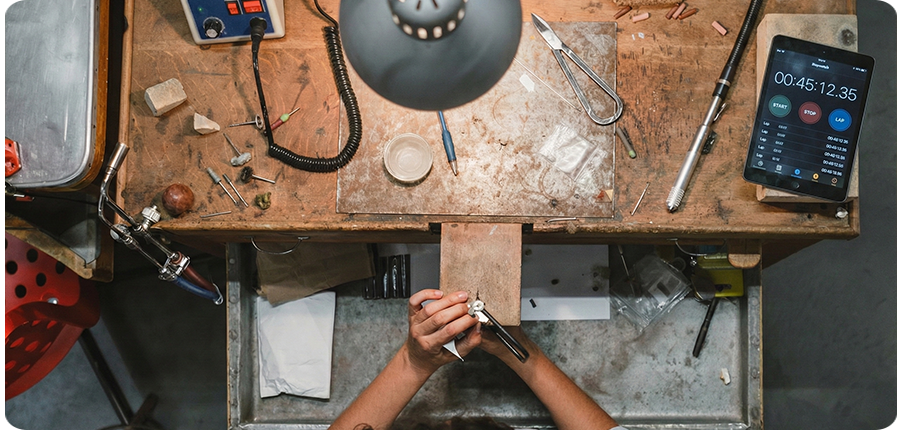 A jeweler working in the workshop, using precision tools and a digital timer to optimize the workflow.