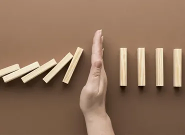 Hand stopping a chain of falling dominoes, representing how to avoid jewelry software implementation failure